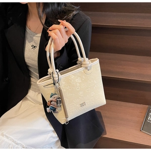 Detail of cream embossed bucket bag with heart patterns and cute teddy bear pendant