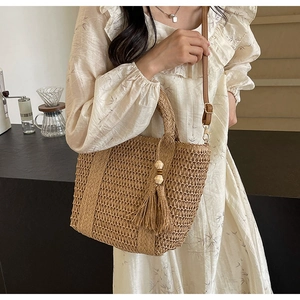 Detail of woven straw tote bag with cutout pattern, bead tassel, and leather strap