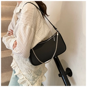 Detail of black textured baguette bag with silver chain on model wearing striped shirt