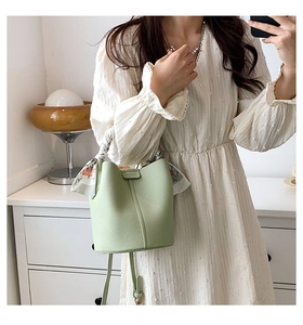 Detail of light green litchi texture bucket bag with silk scarf handle on model