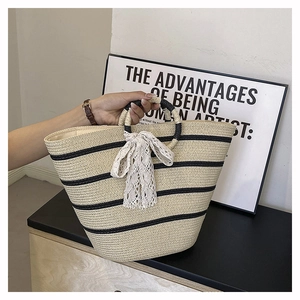 Detail of woven straw tote bag with black stripes and decorative lace scarf handle
