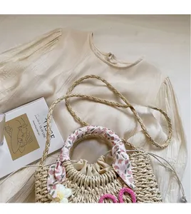 Detail of hand-woven straw beach bag with pink floral scarf and small knit flower decoration