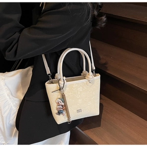 Detail of cream embossed bucket bag with hand-drawn prints and cute 3D bear charm