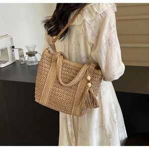Detail of woven straw tote bag featuring reinforced handles and stylish side tassel
