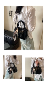 Detailed macro view of black glossy leather boston bag with woven tassel and shoulder strap