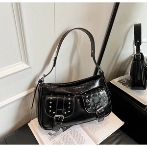 Detail of black patent leather underarm bag with metal studs and buckle pockets
