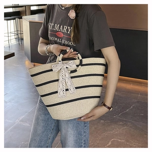Detail of hand-woven straw tote bag with black stripes and white lace bow decoration