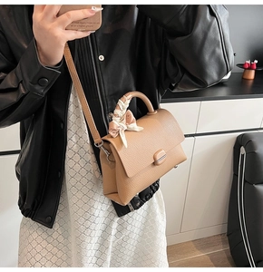 Detail of light brown pebble leather handbag featuring a decorative floral silk scarf on handle