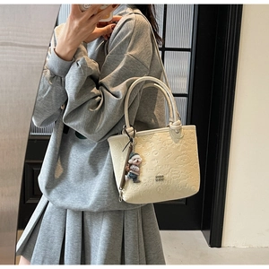 Detail of beige bucket bag featuring cartoon embossing and a cute dog plush charm