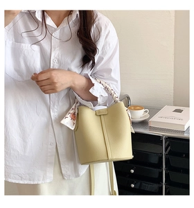 Detail of light yellow leather bucket bag with litchi texture and elegant silk scarf handle