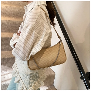 Detail view of light brown woven half-moon baguette bag with silver chain on model
