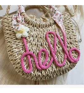 Detail view of woven straw beach bag featuring love embroidery and floral scarf accents