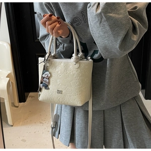 Detail of cream embossed bucket bag with cartoon patterns and cute animal charm