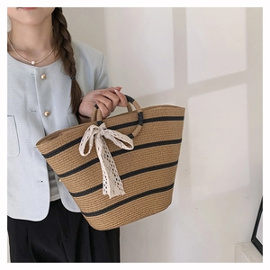 Close-up of woven straw tote bag with navy stripes and a white lace bow detail