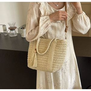 Detail view of woven straw tote bag with brown leather strap and decorative tassel