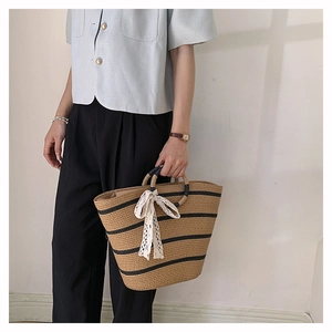 Detail view of woven straw tote bag featuring black stripes and a white lace bow detail