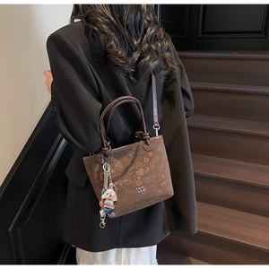 Detail view of brown bucket bag featuring playful doodles and a cute bear bag charm