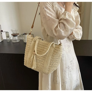 Detail of woven straw tote bag with tassel charm and leather strap on a model
