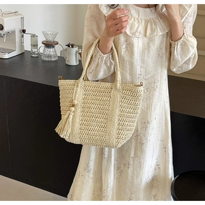 Detail of hand-woven straw tote bag with decorative tassels and wooden beads in cafe setting