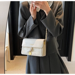 Close-up of white embossed square bag with gold chain strap and metal pendant details