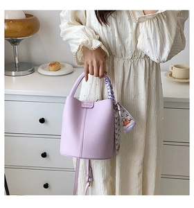 Detail of light purple leather bucket bag with top handle and decorative silk scarf