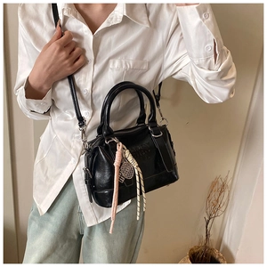 Close-up of black leather Boston bag featuring Enjoy embossed text and woven charm