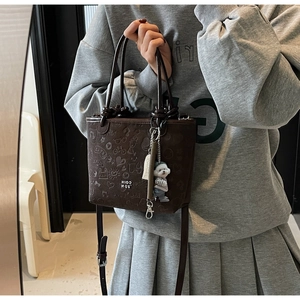 Detail of dark brown embossed bucket bag featuring a cute puppy charm and strap