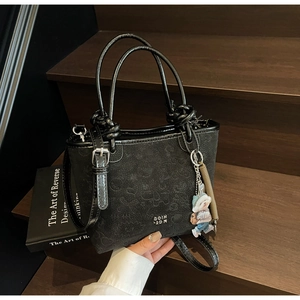 Detail of black embossed tote bag featuring 3D bear charm and knotted handle design