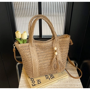 Detail of hand-woven straw tote bag with brown leather strap and tassel on a book