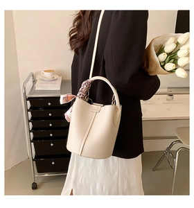 Detail of beige lychee leather bucket bag with a decorative silk scarf on the handle