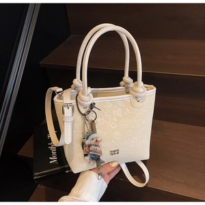 Detail of cream white bucket bag with 3D embossed heart patterns and a cute bear charm