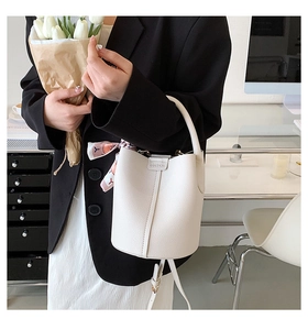 Detailed macro view of a white leather bucket bag featuring a pink floral silk scarf on handle