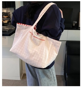 Detailed back view of a white canvas tote bag with red inner plaid pattern and embroidery