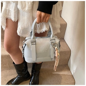 Close-up of light blue soft leather Boston bag with embossed text and woven charm