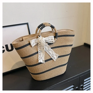 Close-up of woven straw tote bag with black stripes and elegant white lace bow detail