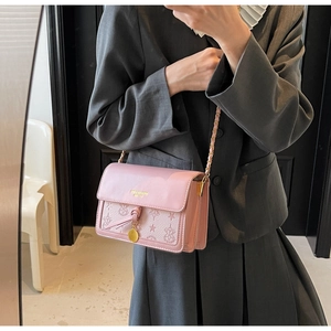 Detail view of pink crossbody bag with embossed floral patterns and golden chain strap
