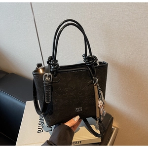 Detail of black embossed bucket bag with cute teddy bear charm and silver metal hardware