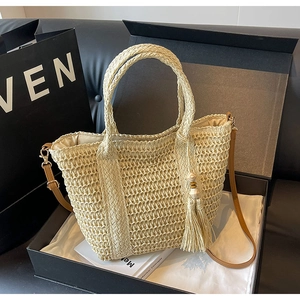 Detail of beige woven tote bag with brown leather strap and wooden bead tassels