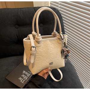 Detail of cream white bucket bag with embossed cartoon patterns and cute pendant charms