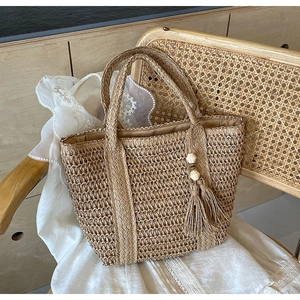 Close-up of woven straw tote bag with decorative tassel and natural fiber texture