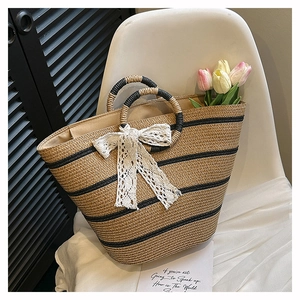 Detail of woven straw tote bag featuring black stripes and a white lace bow ornament