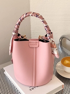Pink litchi grain leather bucket bag with silk scarf handle in cafe setting