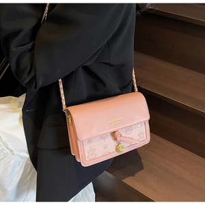 Detail of pink embossed crossbody bag with gold logo and chain strap on a model