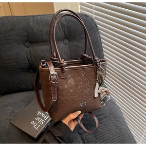 Detailed close-up of dark brown embossed leather bucket bag with cute bear charm detail