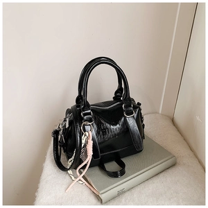 Detail of black glossy Boston bag with embossed text and woven charm on a stylish background