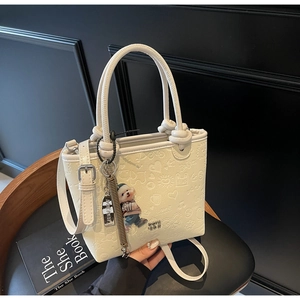 Detail of cream white bucket bag featuring embossed leather patterns and cute bear charm