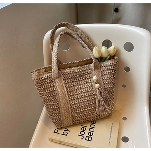 Detailed close-up of handmade woven straw tote bag with elegant tassel and wooden bead decor