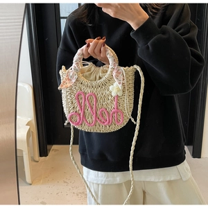 Detail of half-moon straw beach bag with pink hello rope embroidery and flower charm