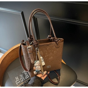 Close-up of brown embossed bucket bag with cute bear charm and metal logo detailing
