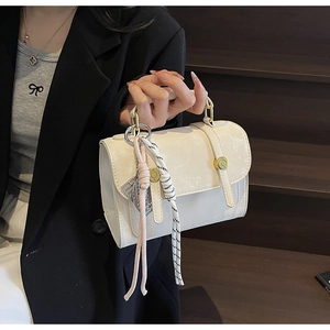 Detail of a beige structured handbag with dual decorative straps and woven rope pendant